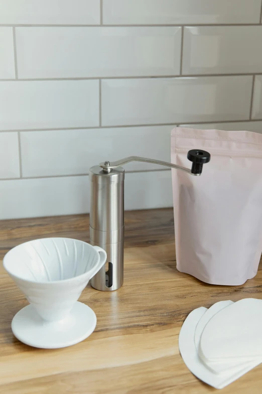 the grinder, bowl, paper bag and coffee cup are sitting on a wooden table