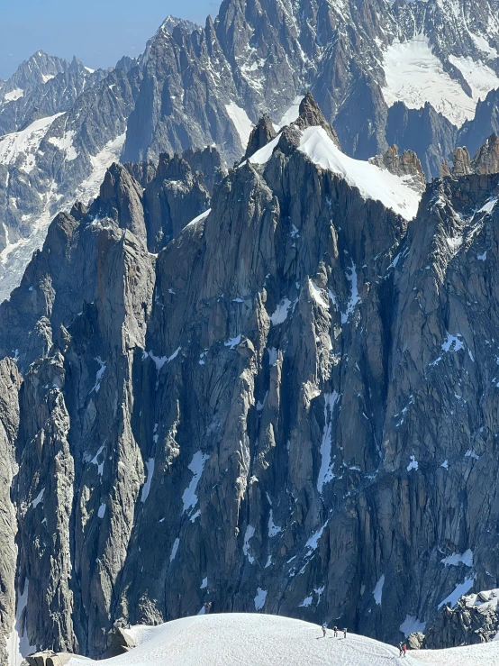 several snow capped mountains sit in the foreground with skiers walking in the distance