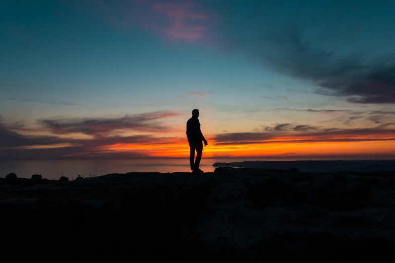 the silhouette of a person walking along a rocky hill