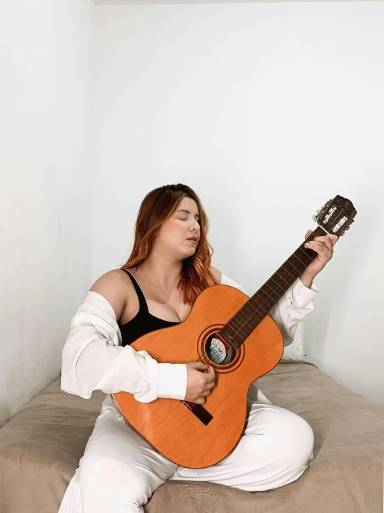 a woman playing a guitar while sitting on a bed