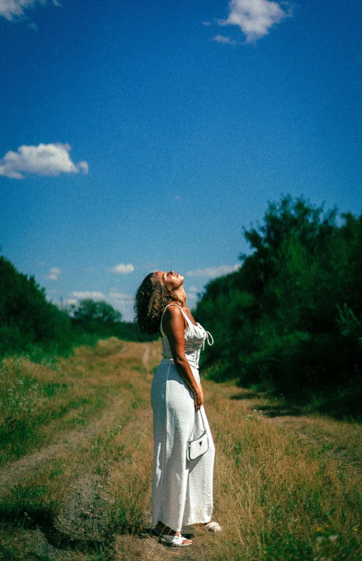 woman in a white dress standing in a dirt road with trees in the background