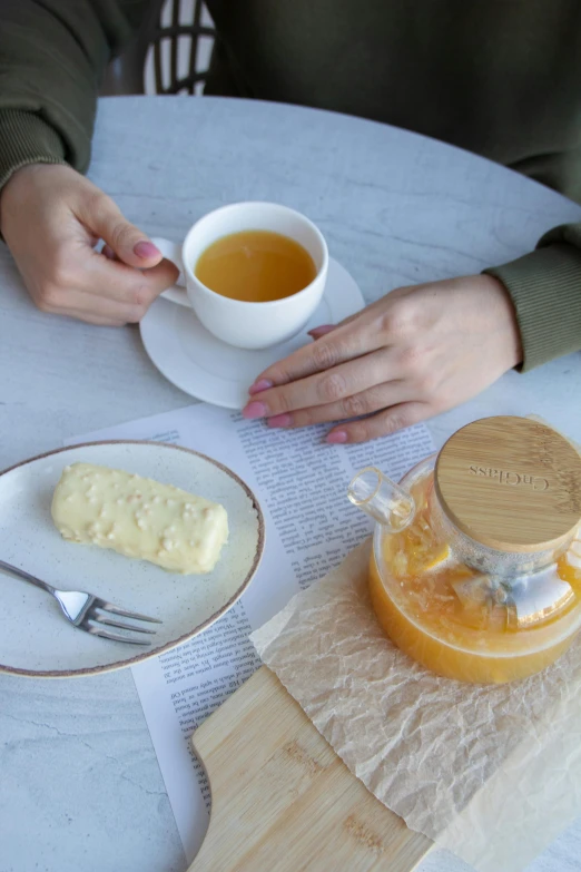 a woman is holding a cup of tea in front of a plate of food