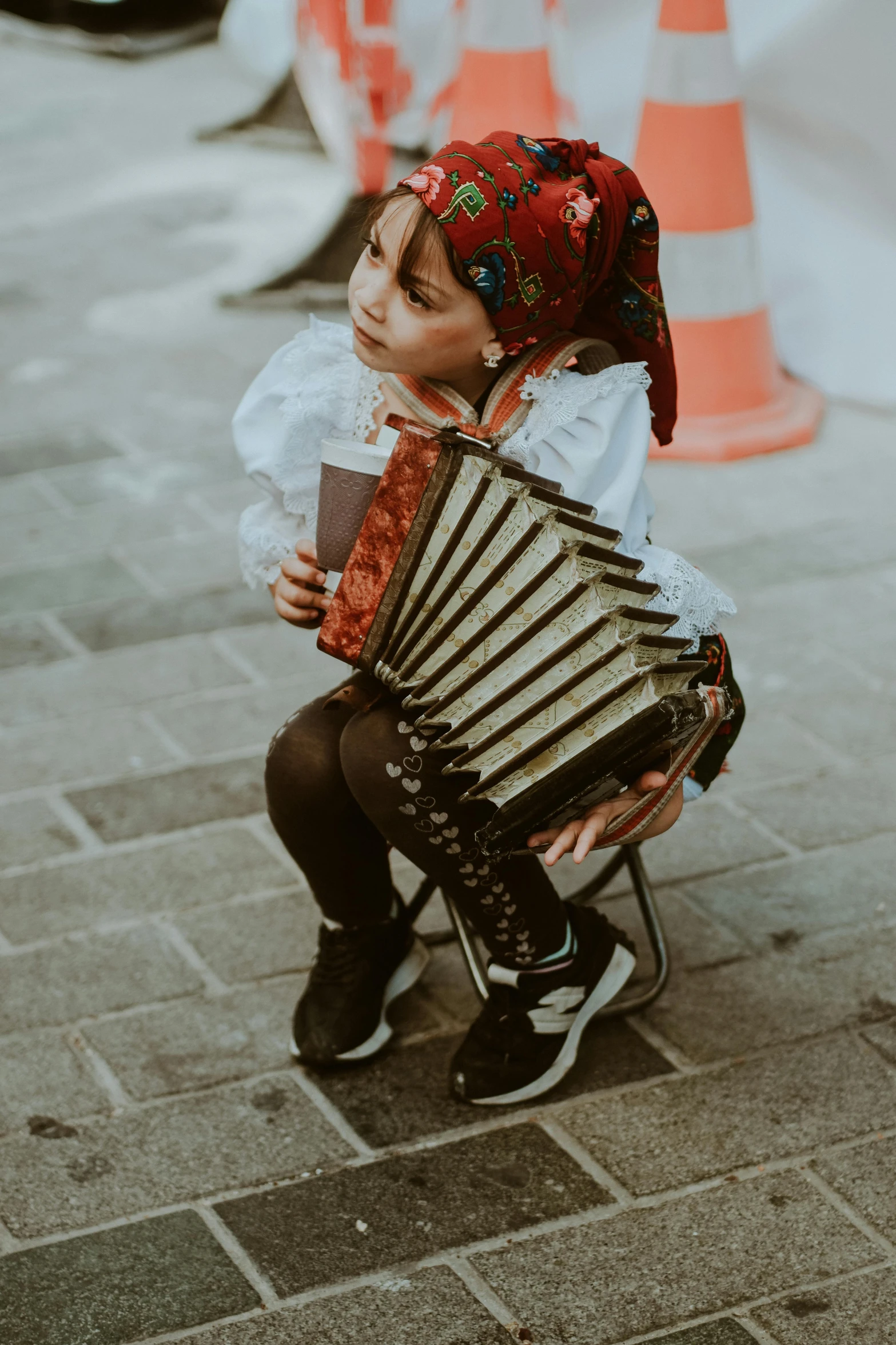  with a patterned head band is sitting on a chair holding a hand held accordion