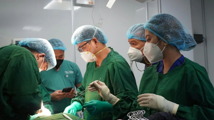 three doctors in green scrubs and masks operating on their electronic devices