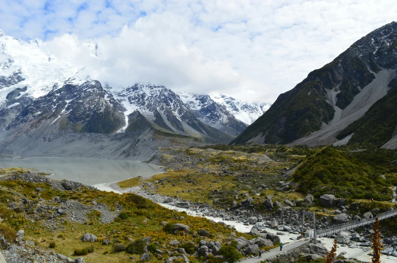 a rocky valley with snow capped mountains and a body of water surrounded by lush greenery