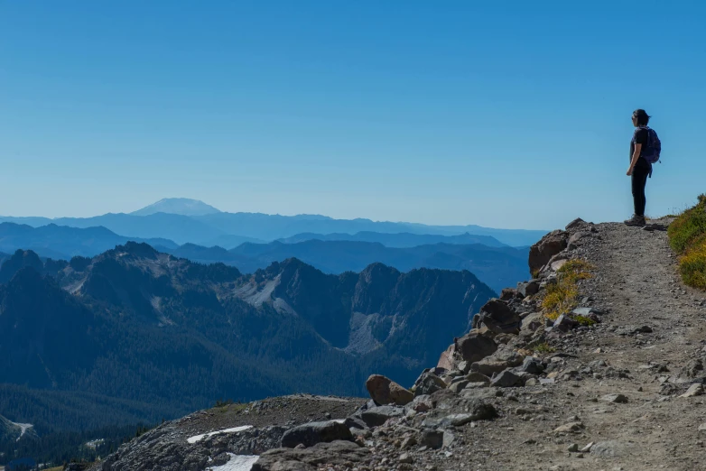 a man stands on a cliff with a view of mountains