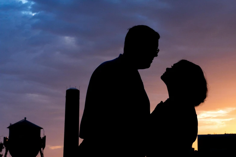 the silhouette of two people standing in front of a sunset