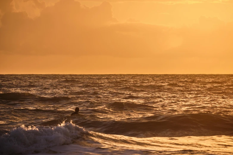 surfer out on the ocean during sunset in front of clouds