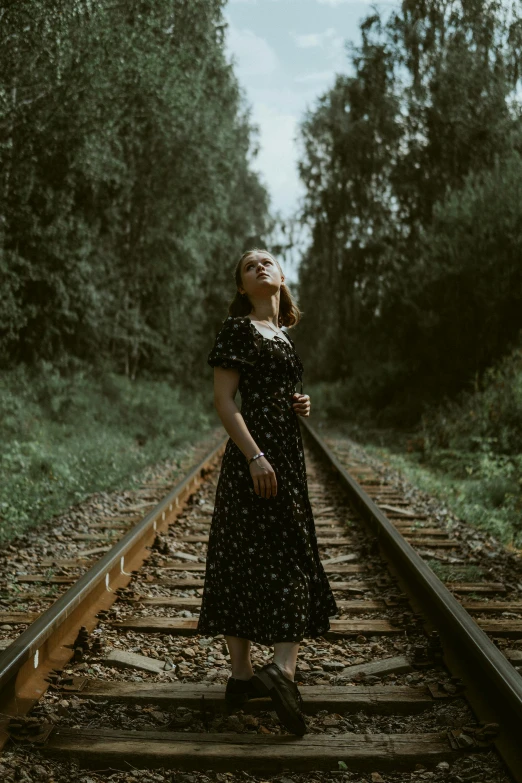 woman standing on train tracks in dress looking up