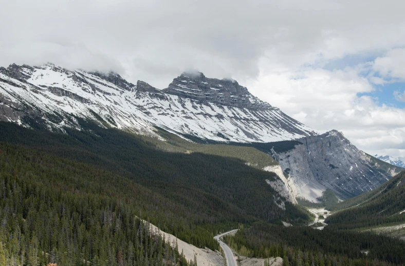 a mountain is covered in snow while road runs beside it