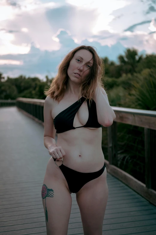 an attractive woman in a black bikini is standing on a pier