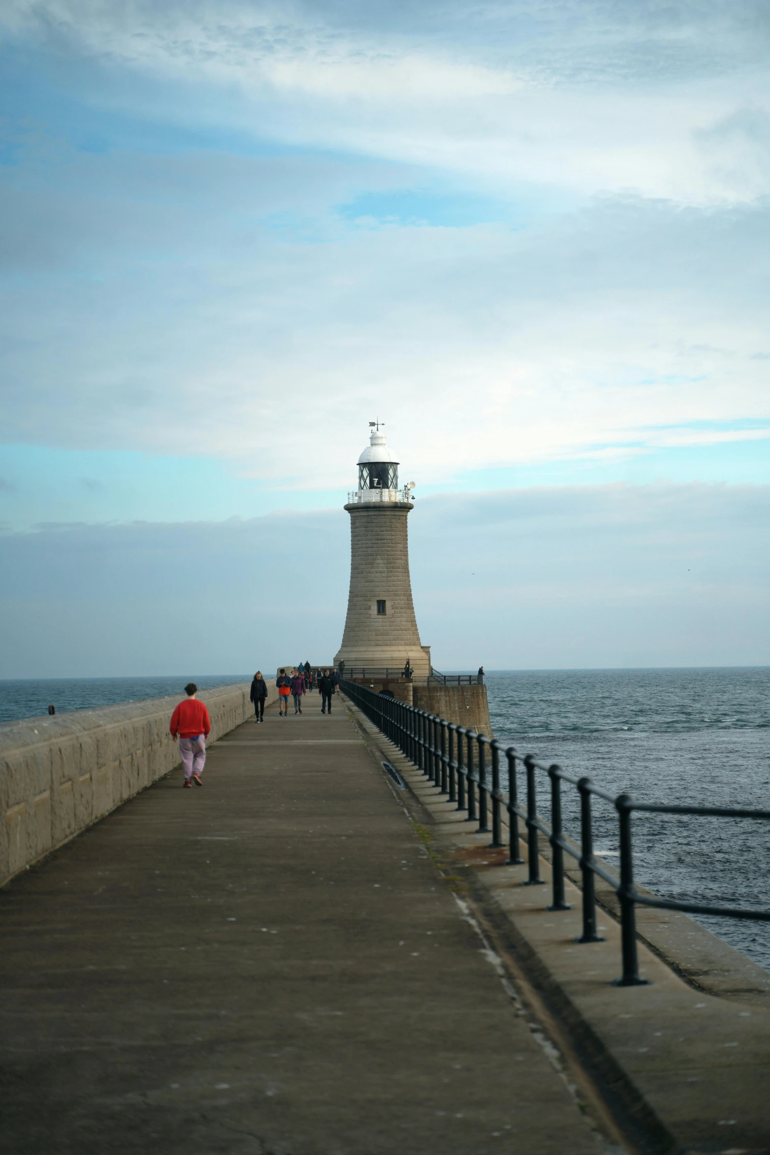 a pier with two people walking on it, with a lighthouse in the distance