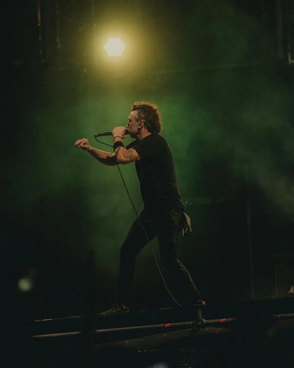 a male singer standing with his arms stretched out with microphone in front of him