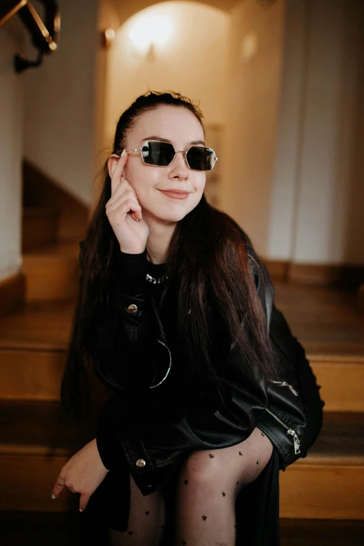 a girl in black leather jacket and sunglasses sitting down