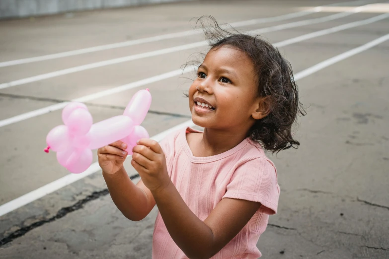 a little girl standing in an empty parking lot holding a bunch of balloons