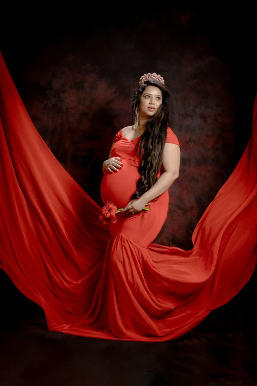 a pregnant woman in a red dress poses with her hands on her hips