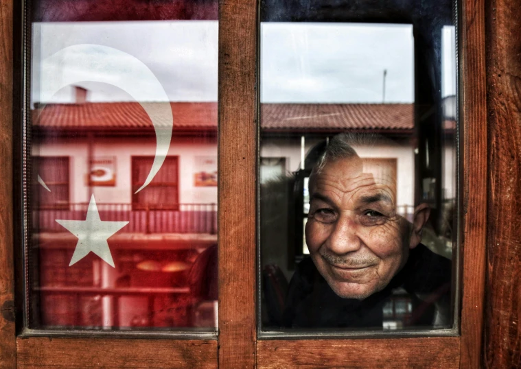 an old man is looking out of a window with the flag of turkey