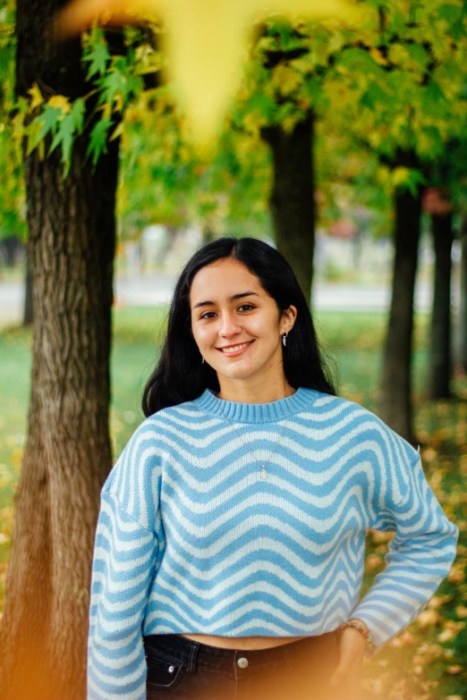 a woman in a sweater in front of trees