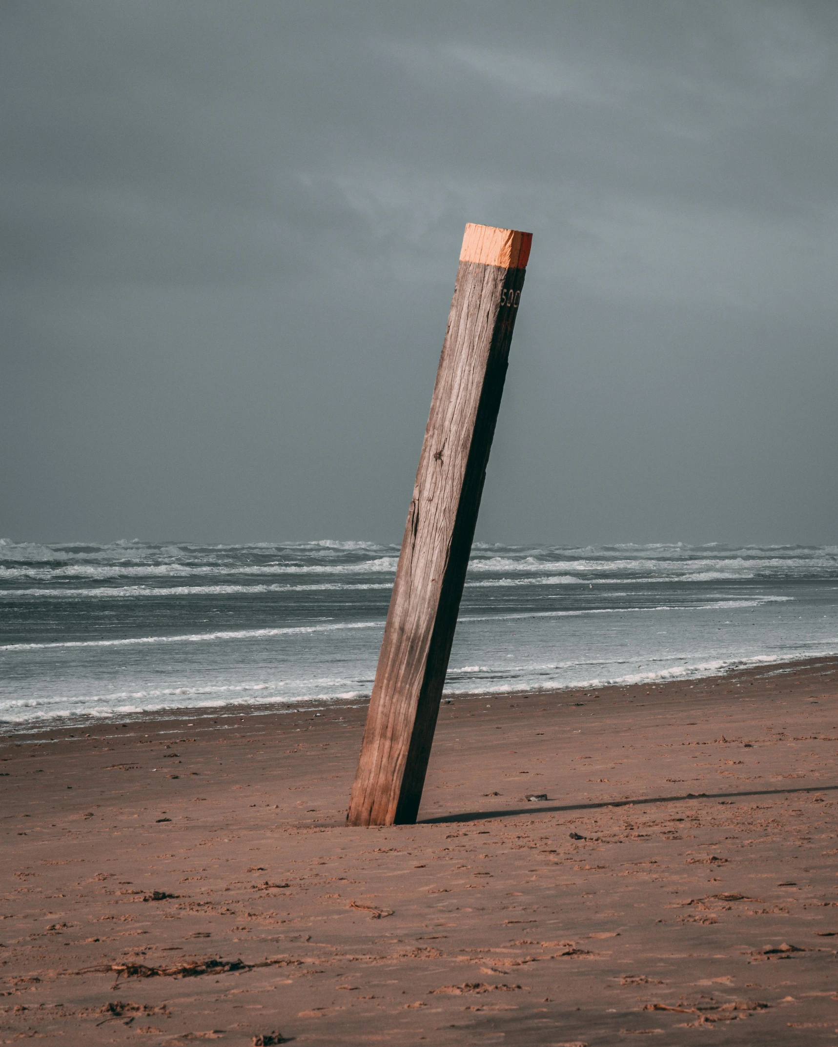 an upturned wooden structure stands on the beach as waves roll in