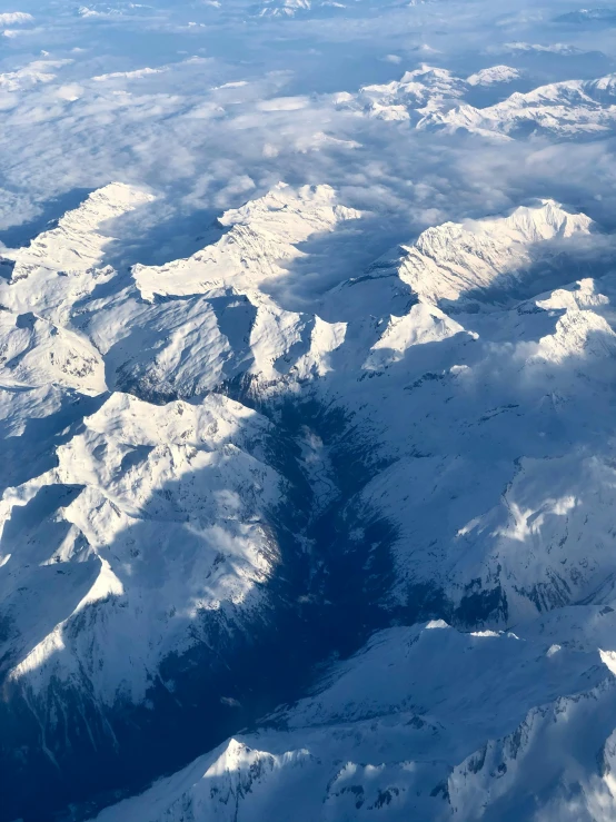 a snowy mountain range with some clouds and the top part of it looking like it has a patch of land in between them