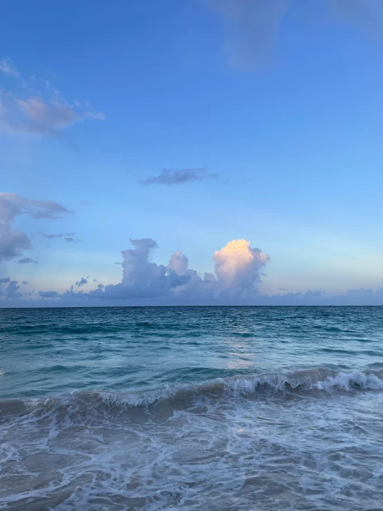 the waves of an ocean with small clouds in the sky