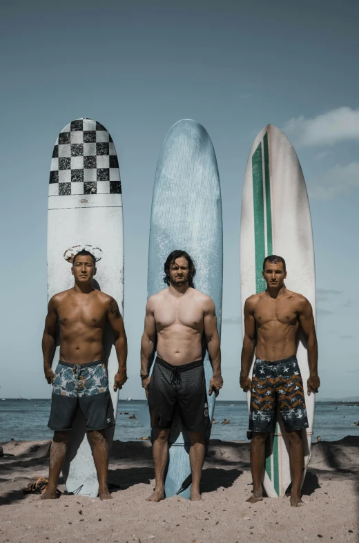 three men standing together in front of two surfboards