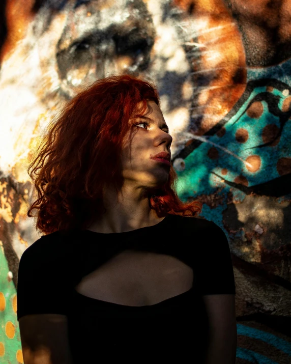 a woman with red hair and eyes closed in front of a colorful painted wall