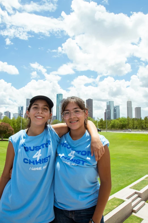 two woman pose for a picture on the grass with the city in the background