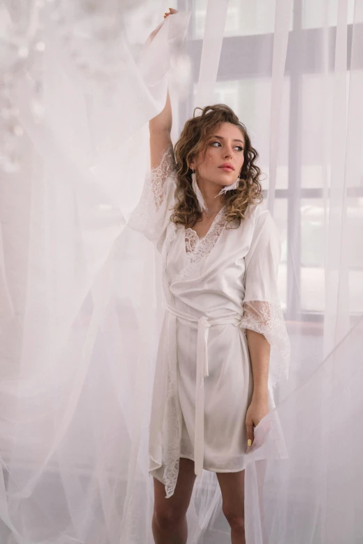 a woman standing next to a white curtain