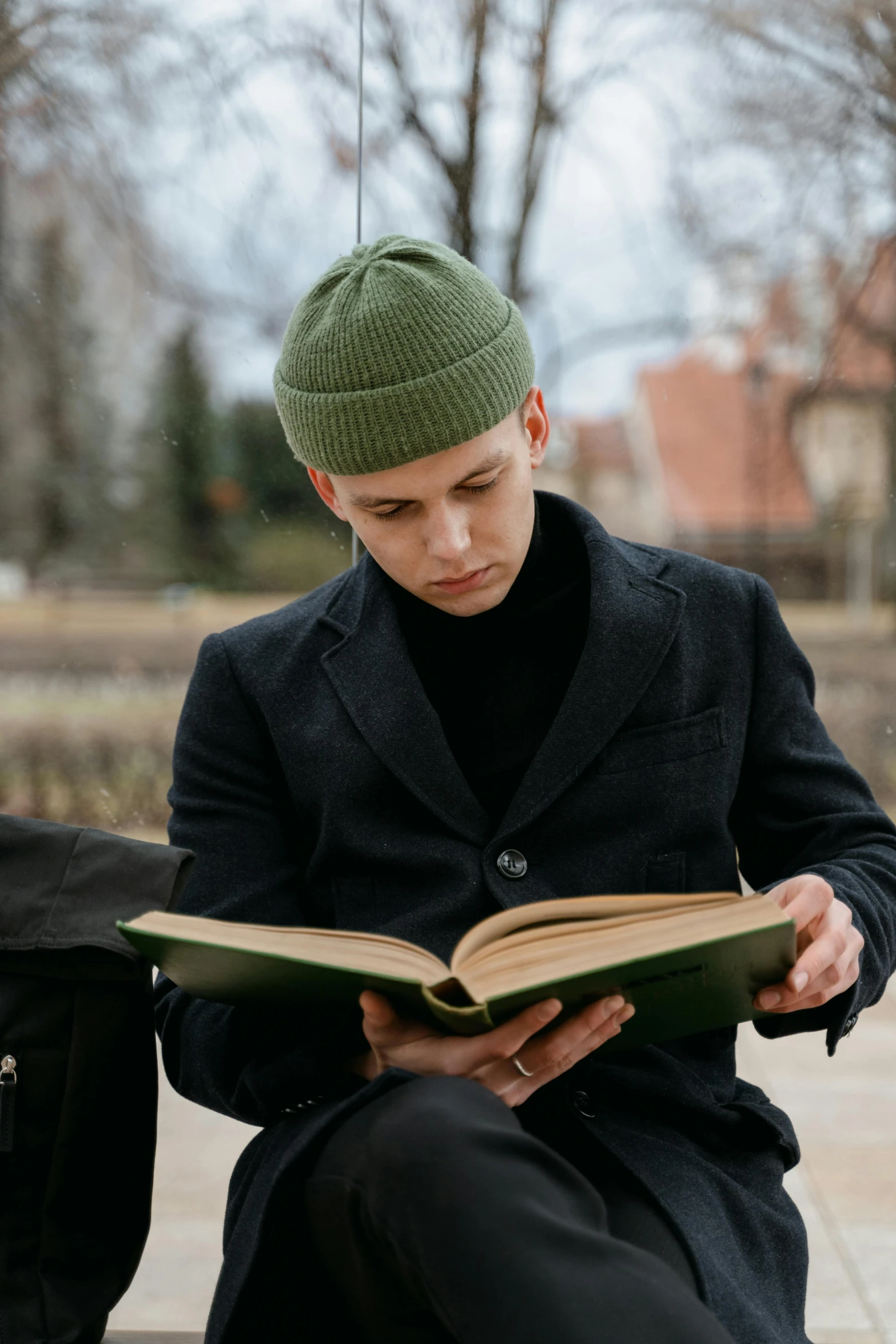 a man sitting on a bench wearing a green hat and reading a book