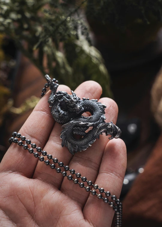 a woman is holding a tiny black dragon pendant