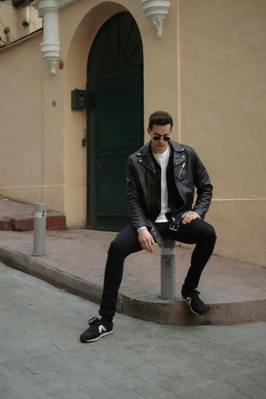 man in black jeans and white shirt sitting on post on sidewalk