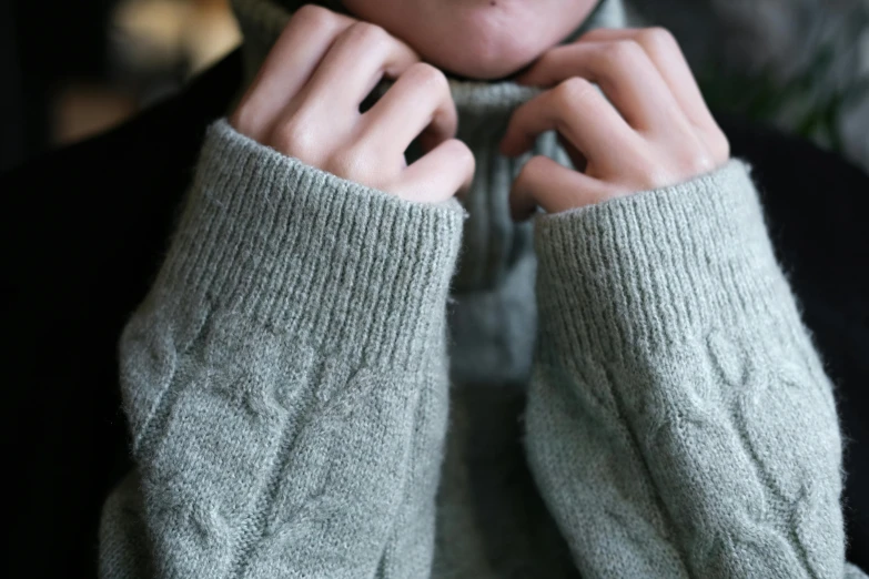 a woman wearing a scarf and a sweater holds her hands together to hear soing