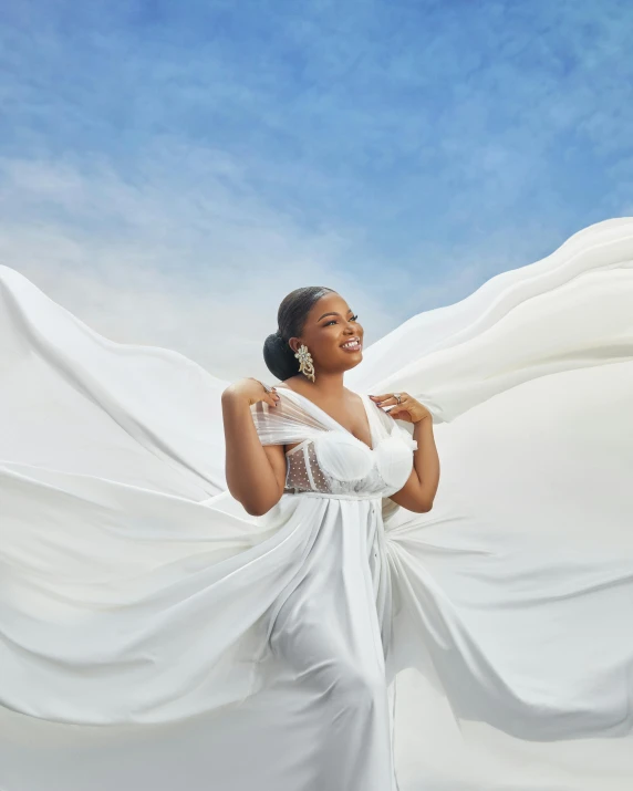 an african american woman in a long white dress holding white cloth over her shoulders