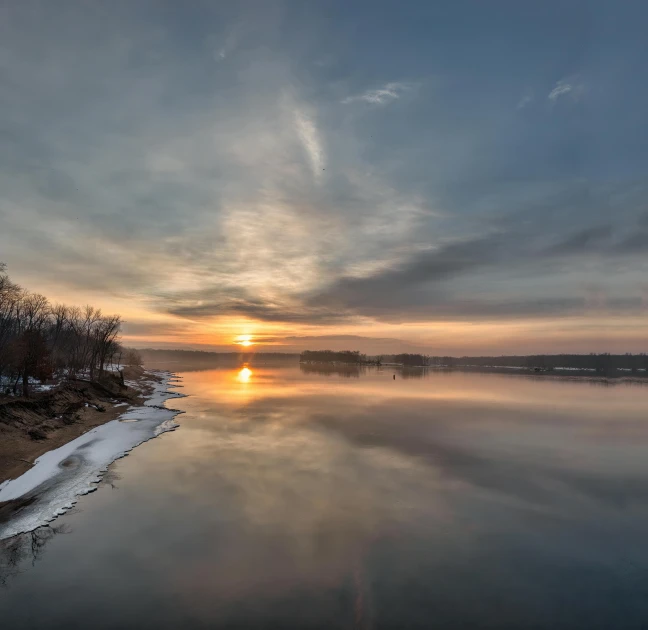 a calm river under a cloudy sky at sunset