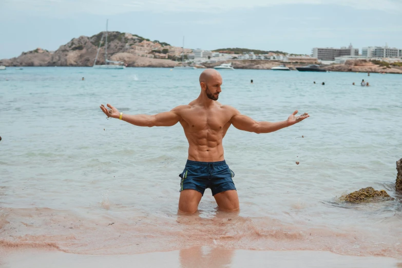 a shirtless man standing in the ocean with arms open