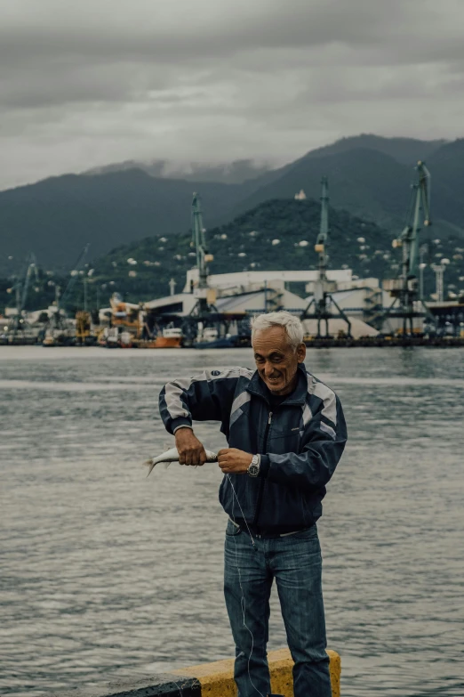 man in black jacket on pier by body of water with large boats