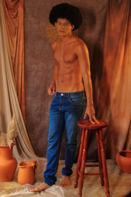 a shirtless young man standing next to a stool and holding his hand on his hip