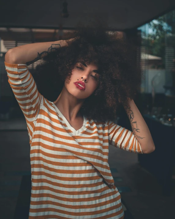 a woman in orange and white striped shirt holds her hair