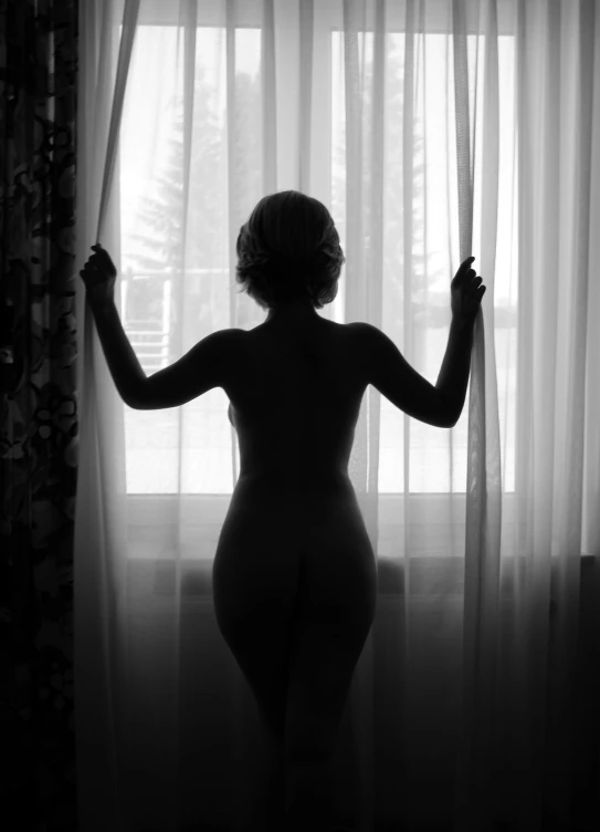 the back view of a  woman in tight - fitting underwear with her hands on curtains