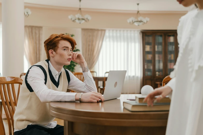 a boy sitting at the table while talking on his cell phone and using his laptop