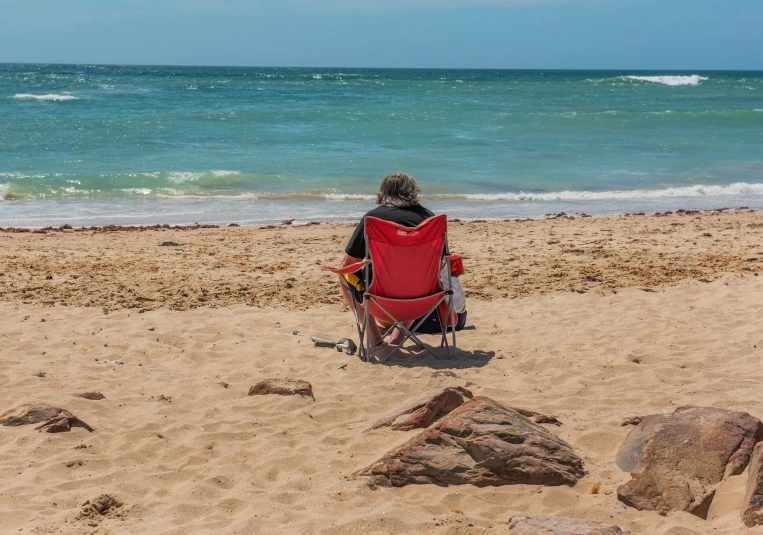 man sitting in chair on sandy beach near ocean