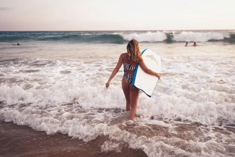 woman holding a surfboard at the beach looking toward waves