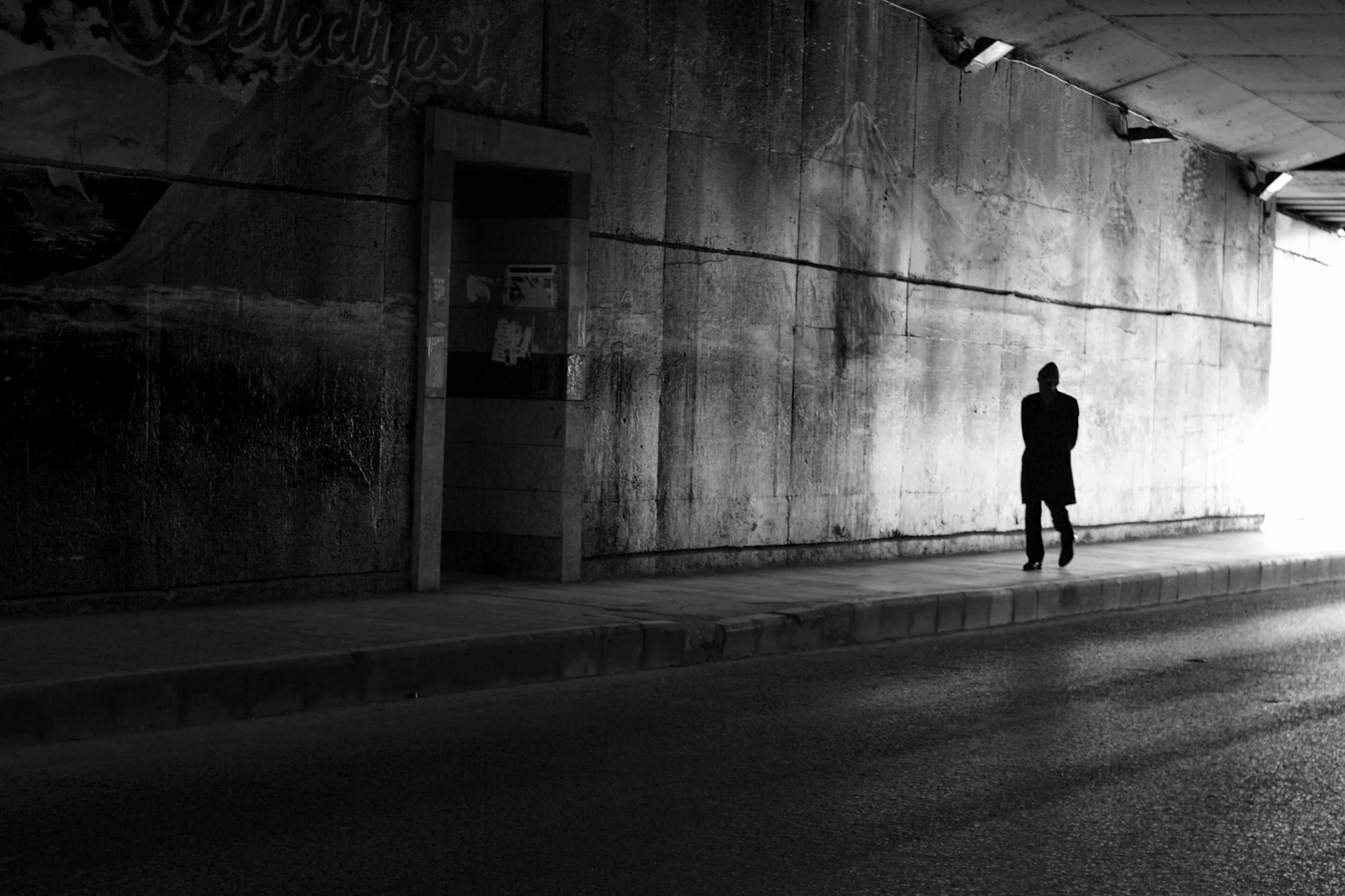 a man standing on the side of a street next to a wall