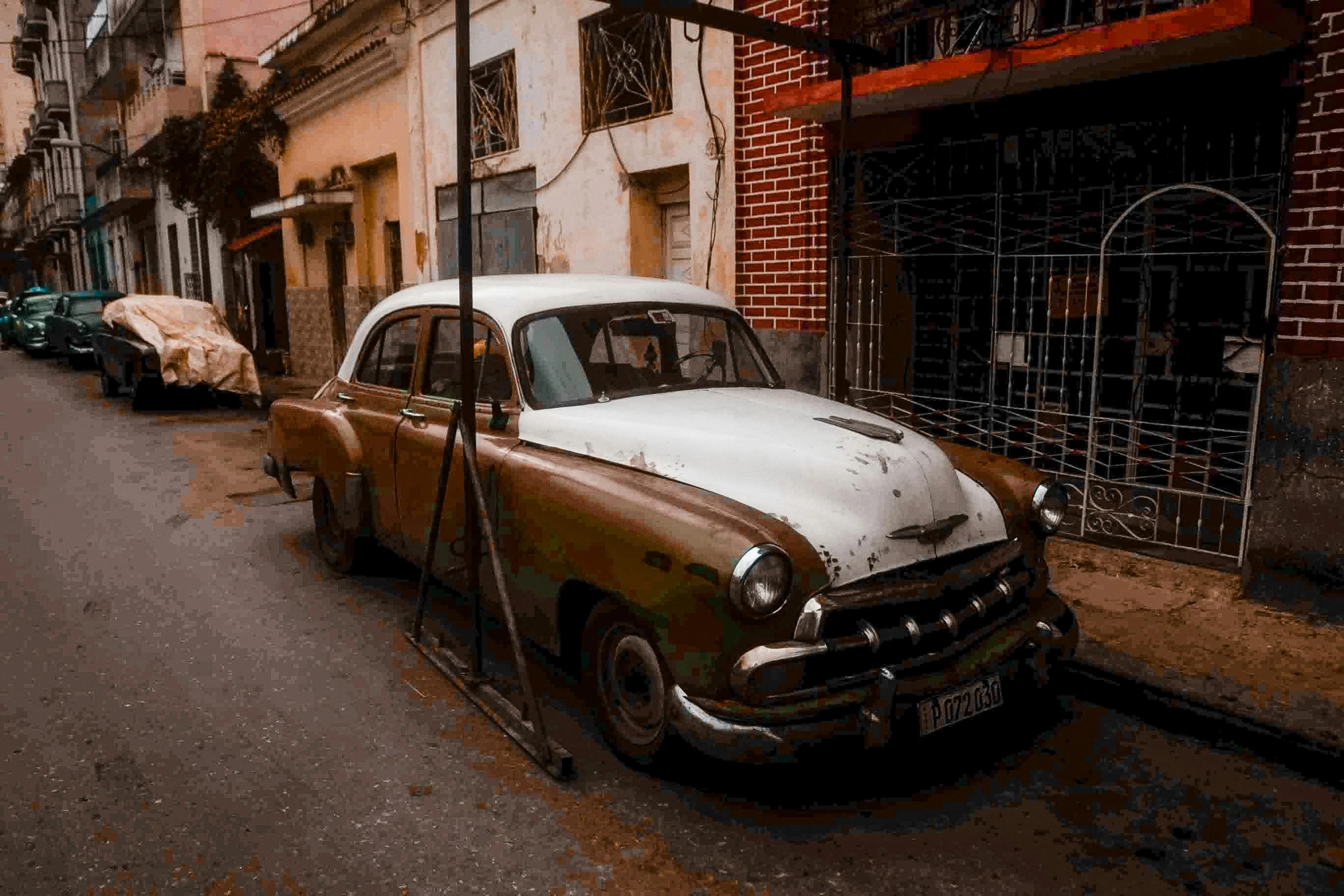 an old, rusted car parked by the side of the street