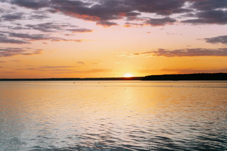 a bright sun rises over the ocean as clouds float above