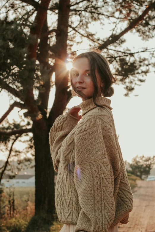 a woman standing in front of a tree wearing a sweater