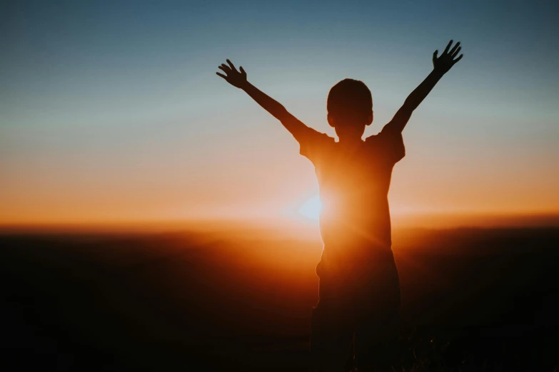 person with arms raised at sun set in the sky