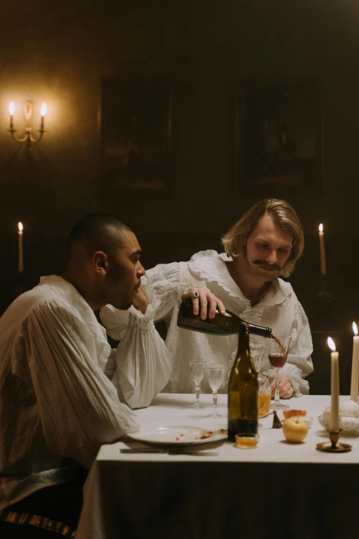 two men sitting around a table and pouring wine