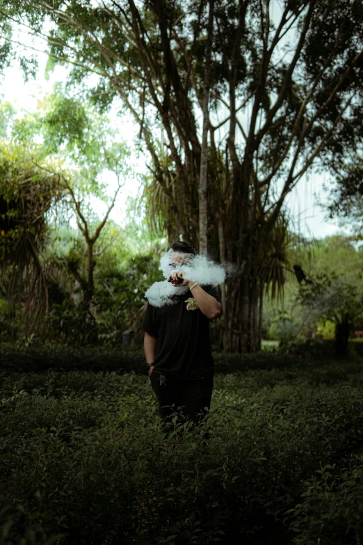 man blowing smoke while walking through grass with trees behind him